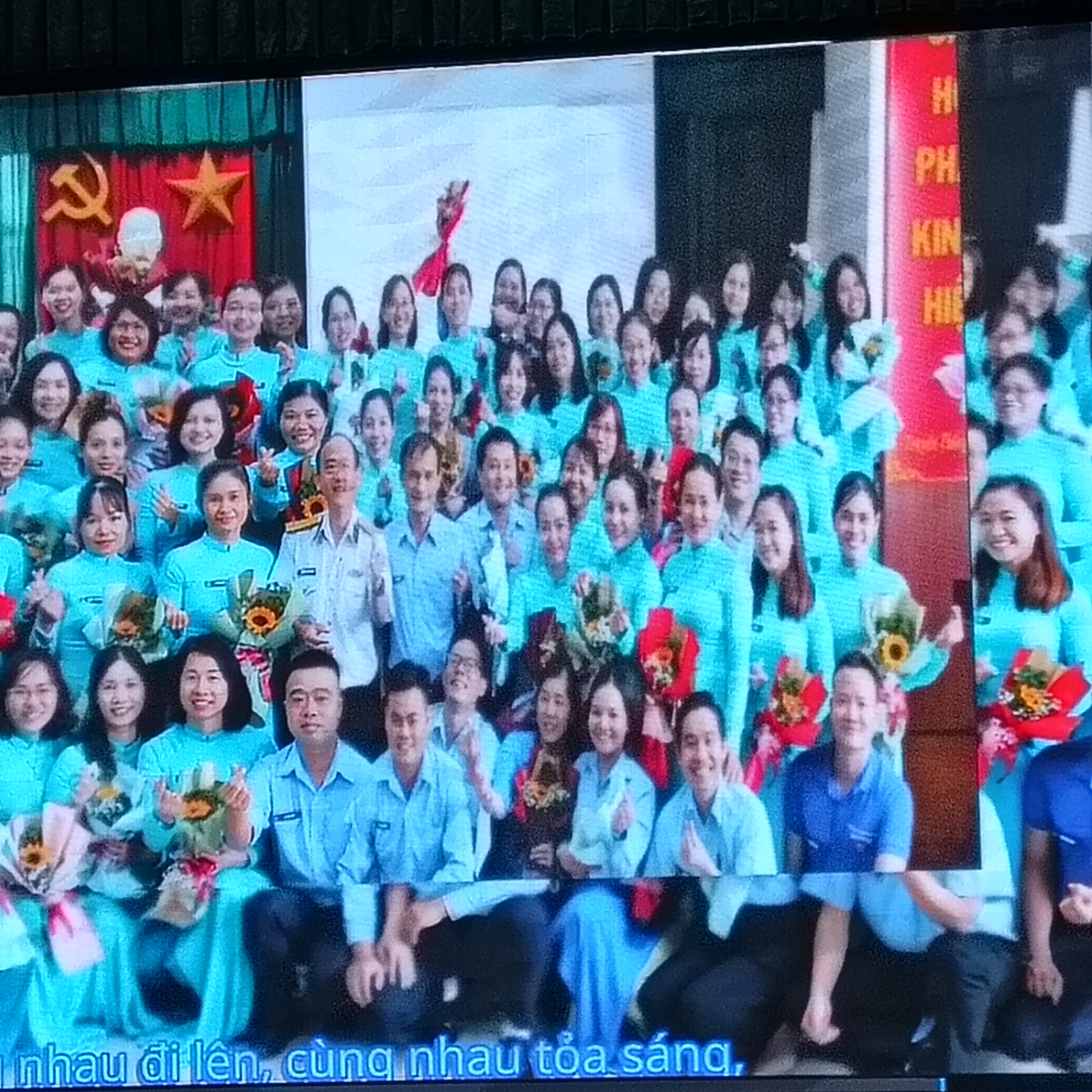 Tiếp tục phim: tập thể nhân viên đồng phục xanh, cờ đỏ sao vàng rực rỡ.